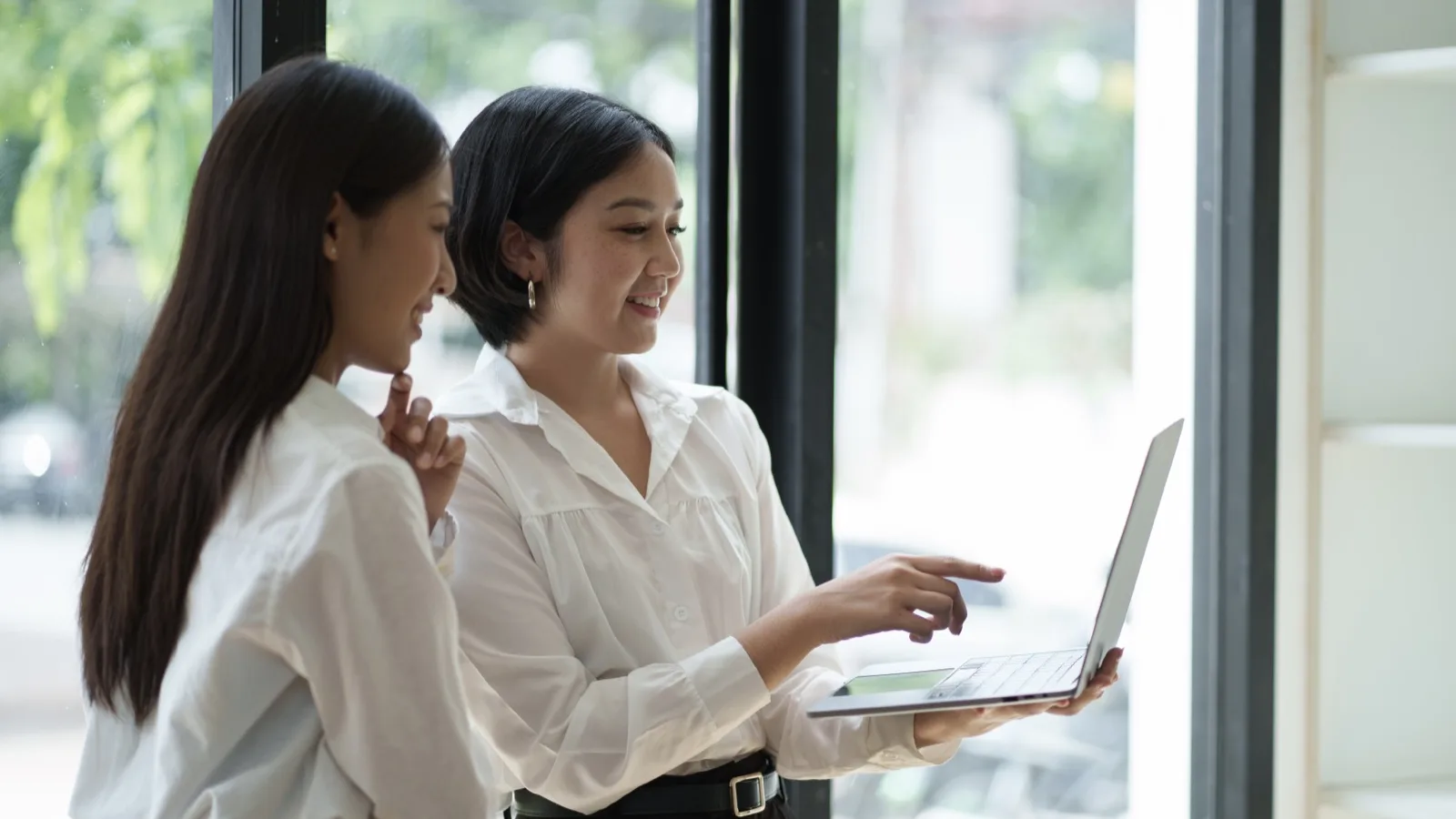 Seen from behind, a woman at an office desk hesitates in front of a monitor showing a cluttered website editor.