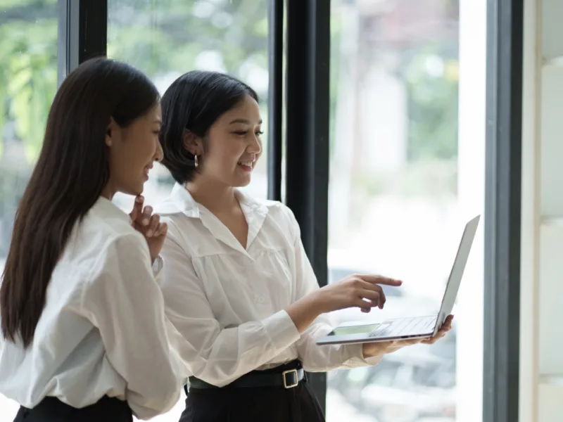 Seen from behind, a woman at an office desk hesitates in front of a monitor showing a cluttered website editor.